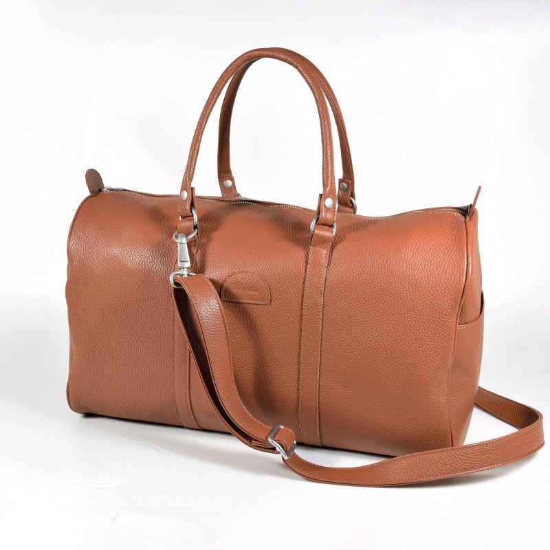 Light-brown leather travel bag on white background, three-quarter view with shoulder strap.
