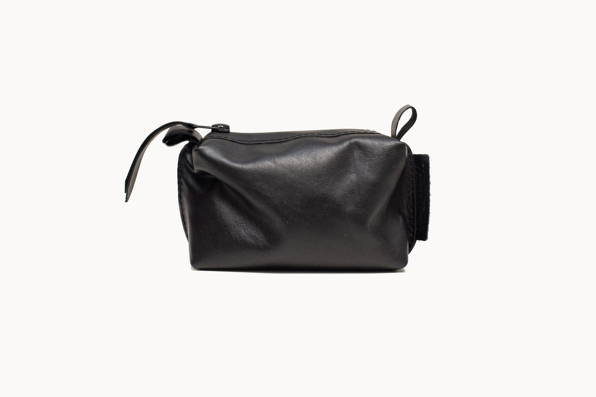 Small black leather cosmetic bag on white background, showing the zip closure and leather pull tab.
