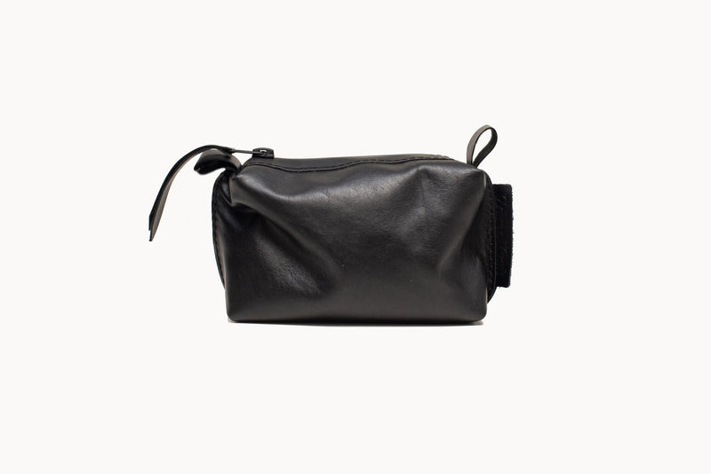 Small black leather cosmetic bag on white background, showing the zip closure and leather pull tab.