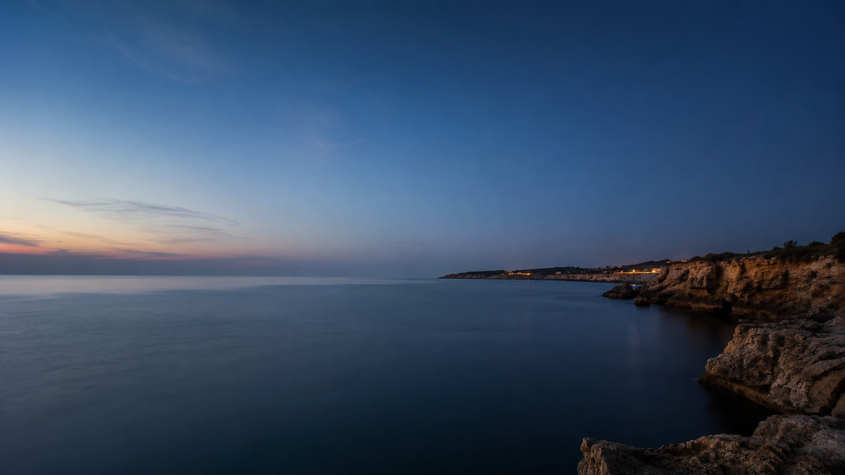 AI-created editorial image: calm Atlantic coastline at dusk with soft haze and distant lights